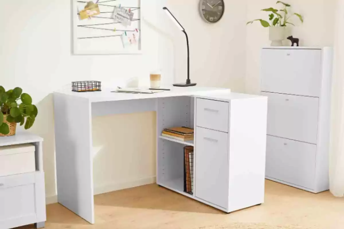 Una oficina a casa amb un escriptori blanc en forma de L, una làmpada de taula negra, una planta en un test, un rellotge de paret, un tauler de notes i un arxivador blanc. Una oficina a casa amb un escriptori blanc en forma de L, una làmpada de taula negra, una planta en un test, un rellotge de paret, un tauler de notes i un arxivador blanc.
