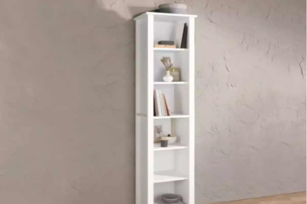 Llibreter blanc d’angle amb diversos prestatges, decorat amb llibres, una planta i alguns objectes petits, col·locat al costat d’una paret de textura rugosa. Llibreter blanc d’angle amb diversos prestatges, decorat amb llibres, una planta i alguns objectes petits, col·locat al costat d’una paret de textura rugosa.