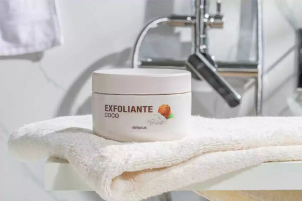 Envàs d'exfoliant de coco sobre una tovallola blanca en un bany.