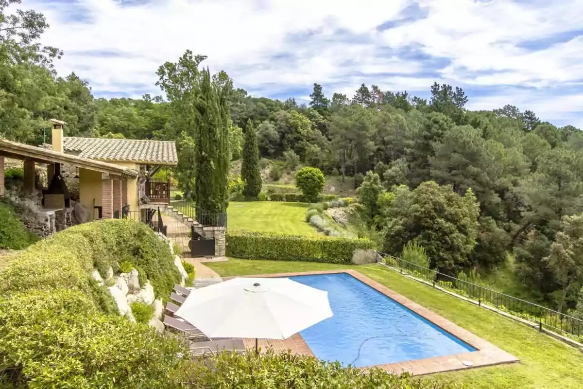 Vista de una casa de campo con piscina rodeada de vegetación y árboles.