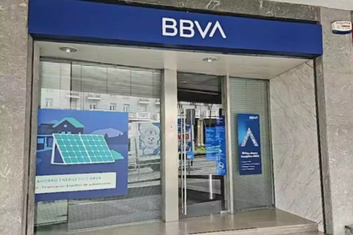 Entrada d'una sucursal del banc BBVA amb cartells promocionals a les finestres.