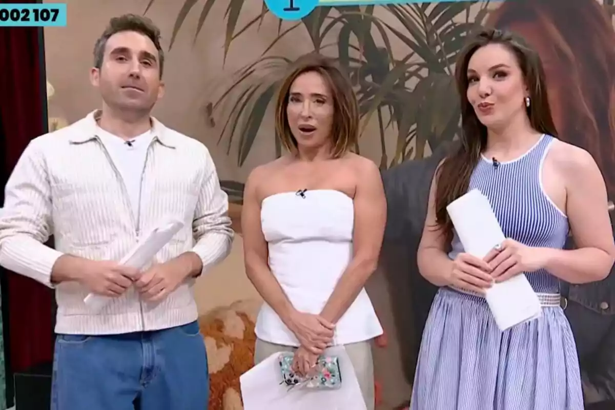 Three television hosts, Aitor Albizua, María Patiño, and Inés Hernand, pose together on a La Familia de la Tele set decorated with plants and a beige background; each holds papers in their hands and they are dressed in casual and elegant clothing. Three television hosts, Aitor Albizua, María Patiño, and Inés Hernand, pose together on a La Familia de la Tele set decorated with plants and a beige background; each holds papers in their hands and they are dressed in casual and elegant clothing.