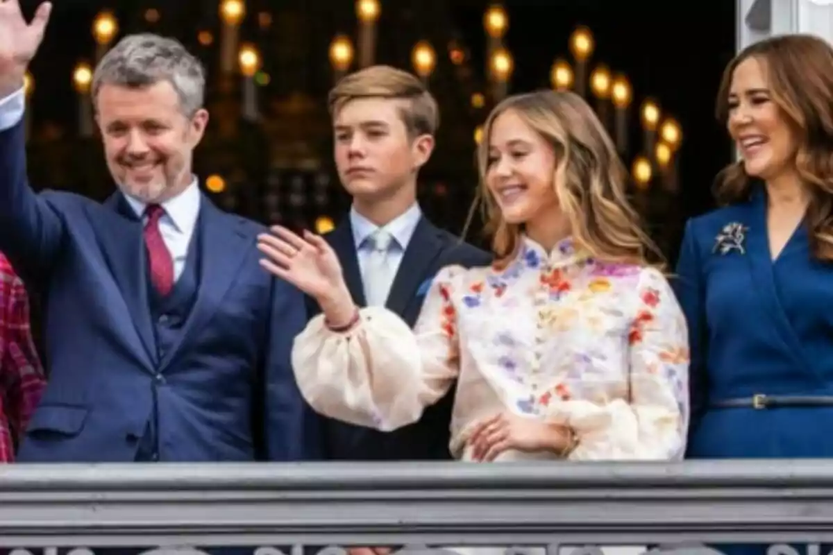 Quatre persones elegantment vestides saluden i somriuen des d’un balcó decorat amb llums al fons. Quatre persones elegantment vestides saluden i somriuen des d’un balcó decorat amb llums al fons.