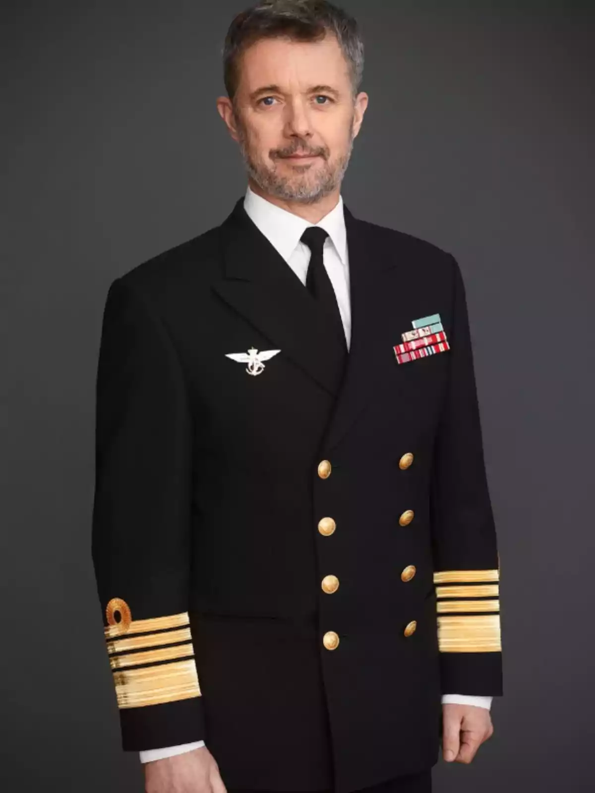 Home de mitjana edat amb barba i cabell curt vestit amb uniforme militar fosc amb botons daurats i condecoracions sobre un fons gris Home de mitjana edat amb barba i cabell curt vestit amb uniforme militar fosc amb botons daurats i condecoracions sobre un fons gris