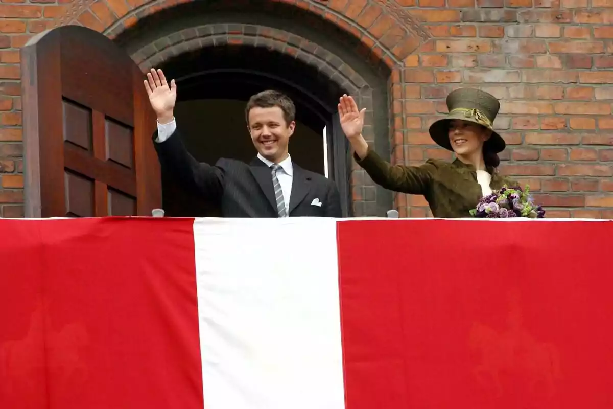 Frederick from Denmark and Mary Donaldon wave from a balcony decorated with a red and white flag.