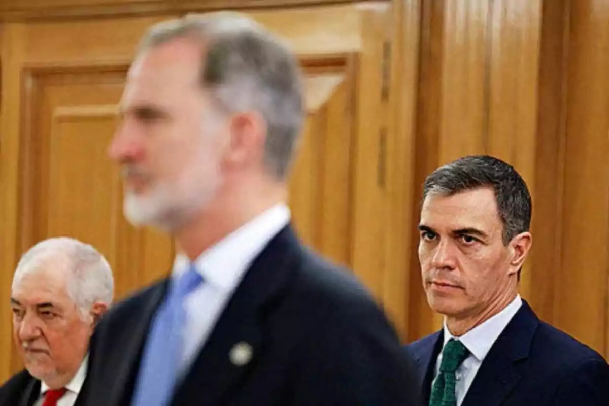 Felip VI i Pedro Sánchez en vestits formals en una sala amb panells de fusta, Felip està desenfocat en primer pla. Felip VI i Pedro Sánchez en vestits formals en una sala amb panells de fusta, Felip està desenfocat en primer pla.