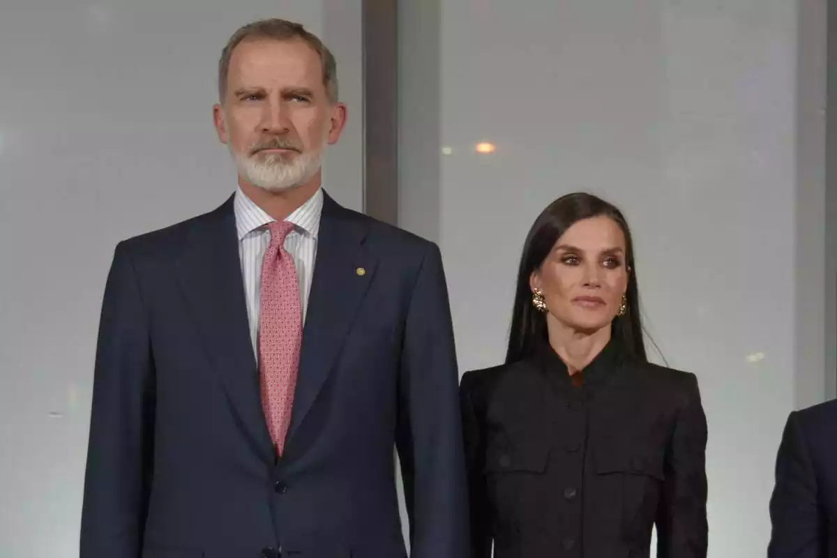 Felip amb corbata vermella i Letizia vestida de negre seriosos mirant de banda