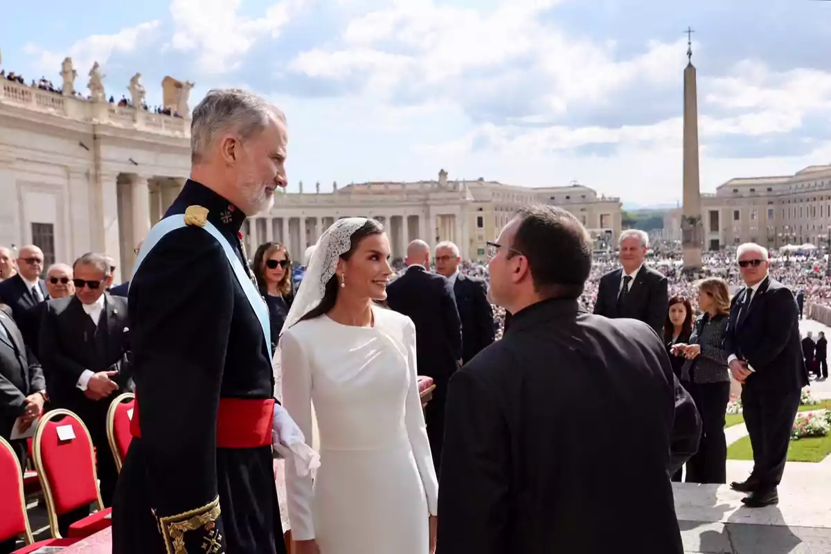 Felipe i Letizia elegantment vestits conversen amb un sacerdot en una plaça concorreguda amb arquitectura clàssica de fons. Felipe i Letizia elegantment vestits conversen amb un sacerdot en una plaça concorreguda amb arquitectura clàssica de fons.