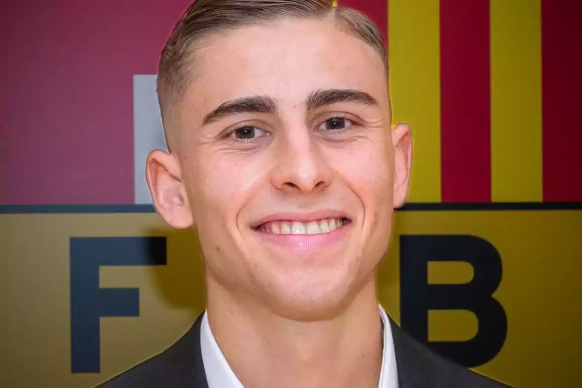 A young man smiling in front of a background with red and yellow letters and colors.