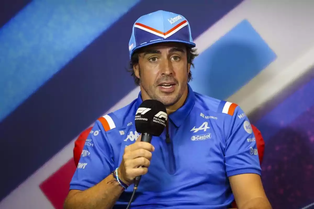 Un hombre con gorra y camiseta azul sostiene un micrófono durante una conferencia de prensa. Un hombre con gorra y camiseta azul sostiene un micrófono durante una conferencia de prensa.