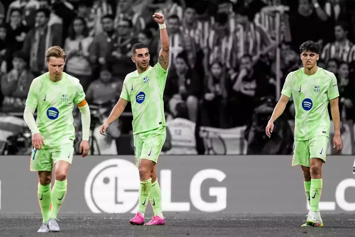 Soccer players in green uniforms on the field, one of them raising his arm, with the crowd in the background in black and white. Soccer players in green uniforms on the field, one of them raising his arm, with the crowd in the background in black and white.