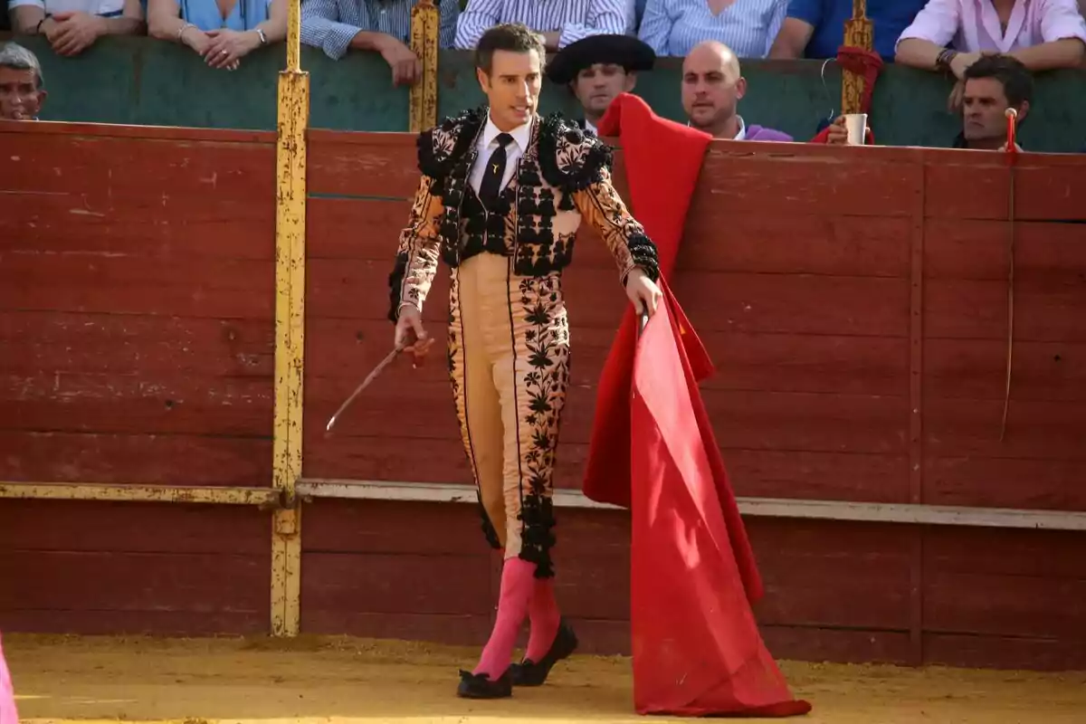 Finito de Còrdova a la plaça de toros sostenint una crossa vermella mentre el públic observa des de les grades. Finito de Còrdova a la plaça de toros sostenint una crossa vermella mentre el públic observa des de les grades.