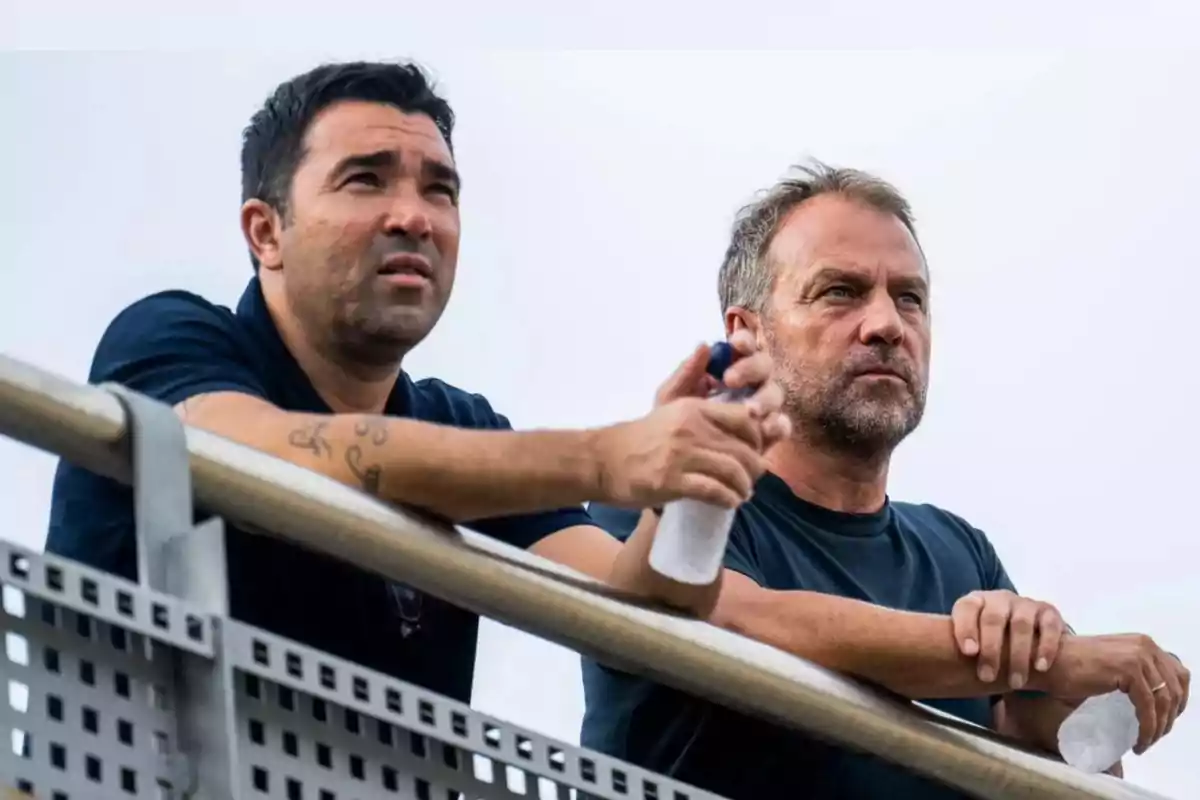 Dos hombres observando desde una barandilla mientras sostienen botellas de agua.