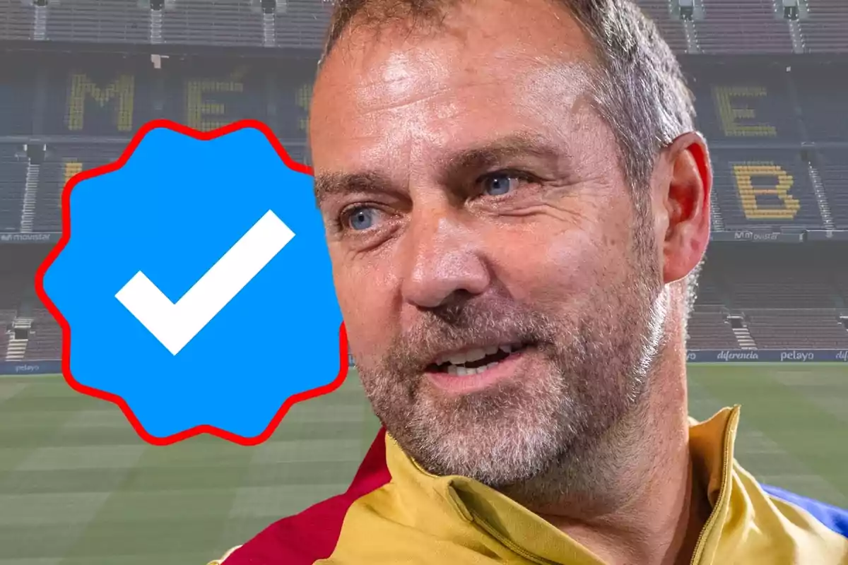 Un home somrient amb barba i cabells curts en un estadi de futbol amb un símbol de verificació blava al costat.