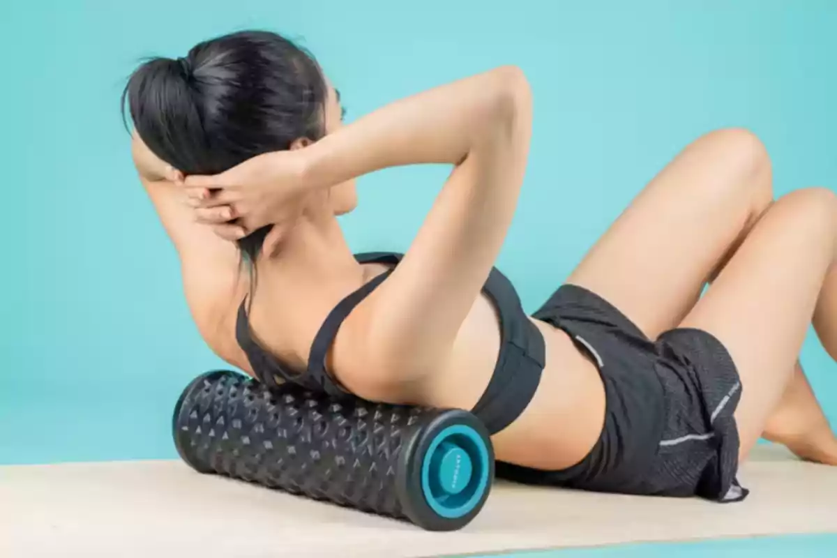 Dona fent exercici amb un corró d'escuma sobre un matalàs. Dona fent exercici amb un corró d'escuma sobre un matalàs.