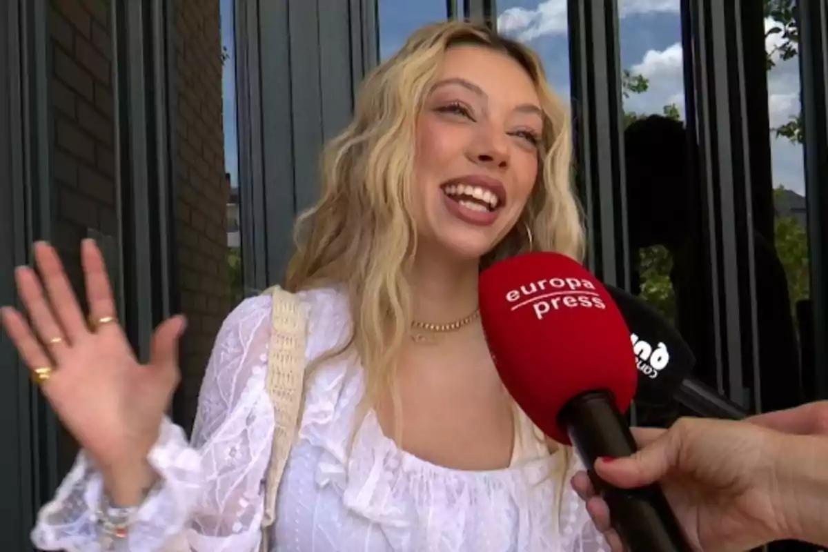 Alejandra Rubio somrient amb una brusa blanca sent entrevistada per un micròfon vermell d’Europa Press mentre saluda amb la mà Alejandra Rubio somrient amb una brusa blanca sent entrevistada per un micròfon vermell d’Europa Press mentre saluda amb la mà