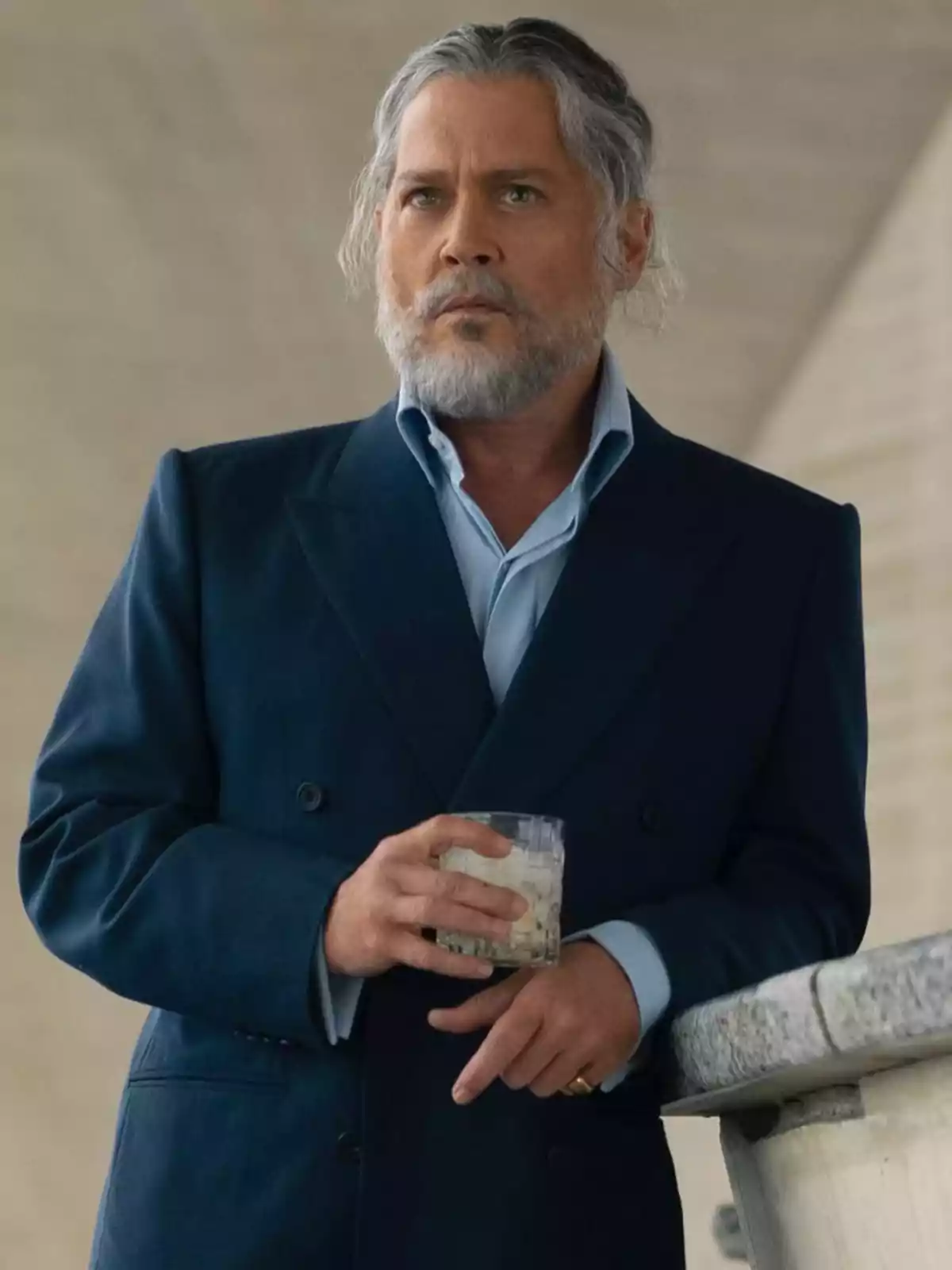 Johnny Depp de cabells canosos i barba vestit amb un vestit blau, sostenint un got a la mà mentre està recolzat en una barana