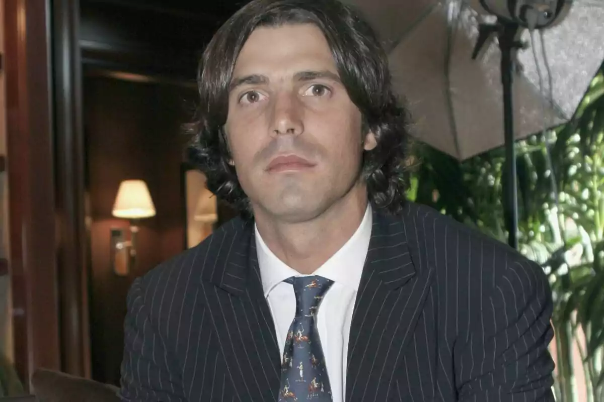 Nacho Figueras amb vestit de ratlles i corbata està assegut en un ambient interior amb il·luminació càlida i plantes al fons.