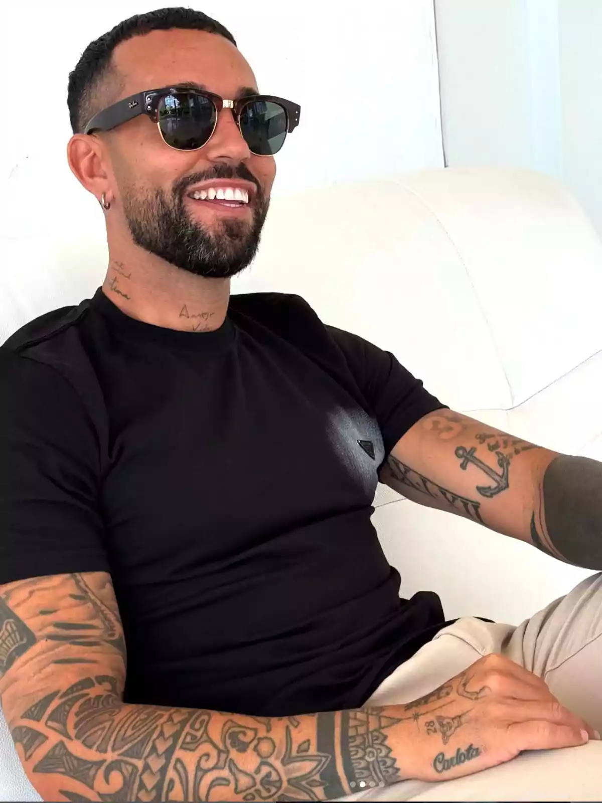 Omar Sánchez amb barba i ulleres de sol assegut en un sofà blanc, porta una samarreta negra i té diversos tatuatges als braços i al coll. Omar Sánchez amb barba i ulleres de sol assegut en un sofà blanc, porta una samarreta negra i té diversos tatuatges als braços i al coll.