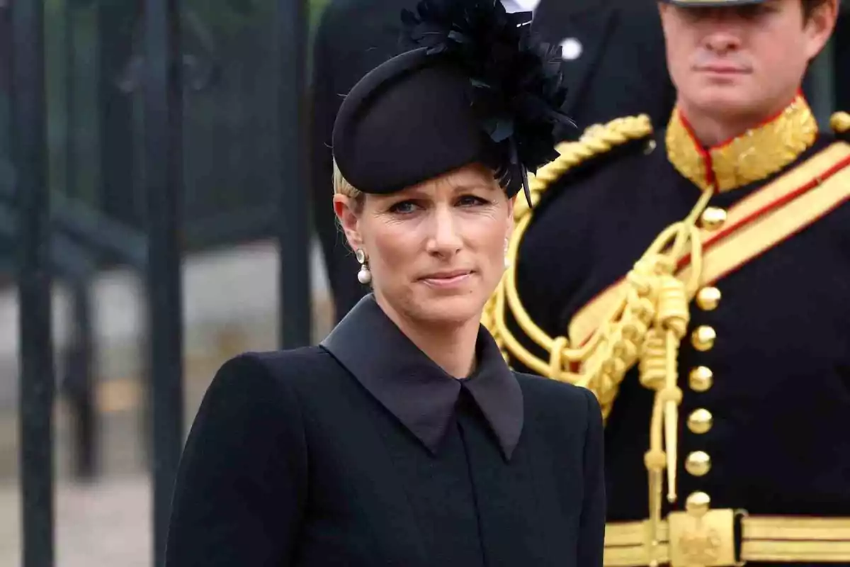 Zara Tindall amb barret negre i vestit formal està dreta al costat d'un home amb uniforme militar. Zara Tindall amb barret negre i vestit formal està dreta al costat d'un home amb uniforme militar.