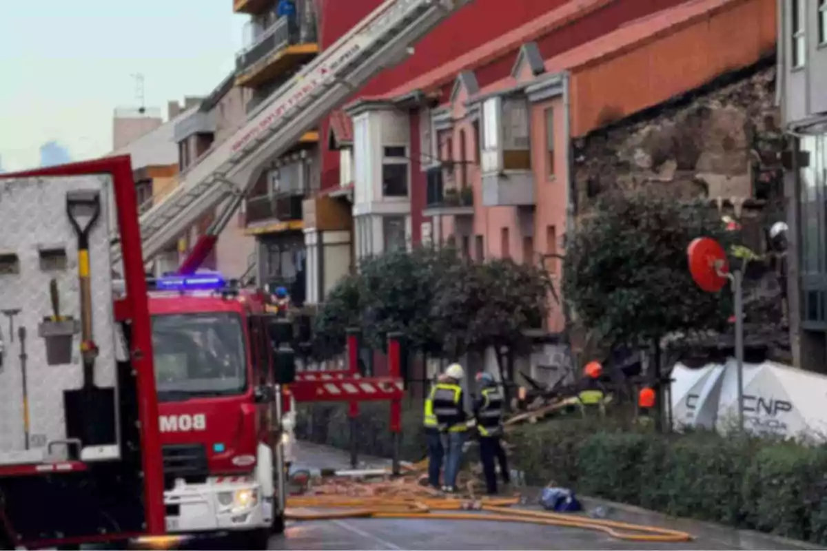 Bombers treballant a l'escena d'un esfondrament en un edifici residencial amb un camió de bombers i una escala estesa.