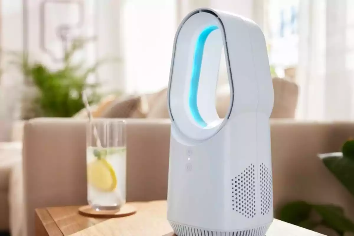 Ventilador modern sense aspes sobre una taula al costat d’un got d’aigua amb una rodanxa de llimona en una sala il·luminada.