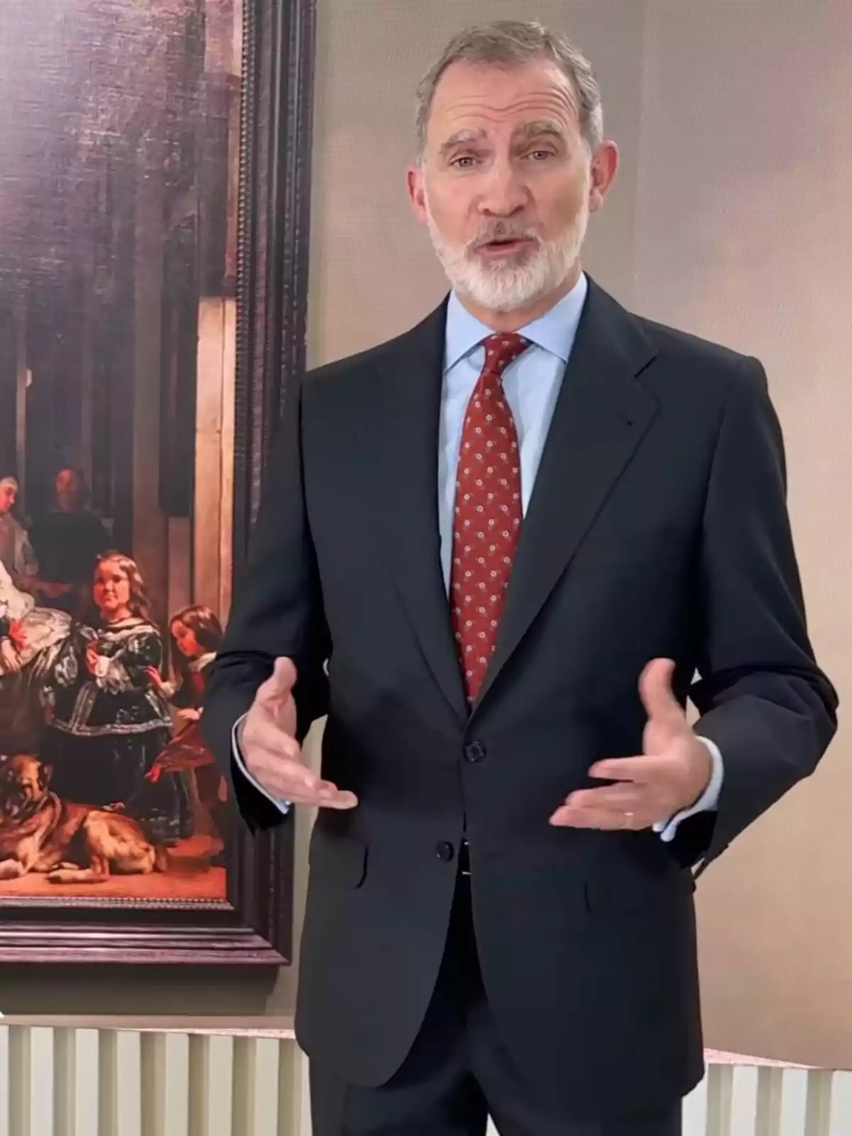 El rei Felip VI de cabells canosos i barba vestit amb un vestit fosc i corbata vermella posant davant de 'Las meninas' de Velázquez El rei Felip VI de cabells canosos i barba vestit amb un vestit fosc i corbata vermella posant davant de 'Las meninas' de Velázquez