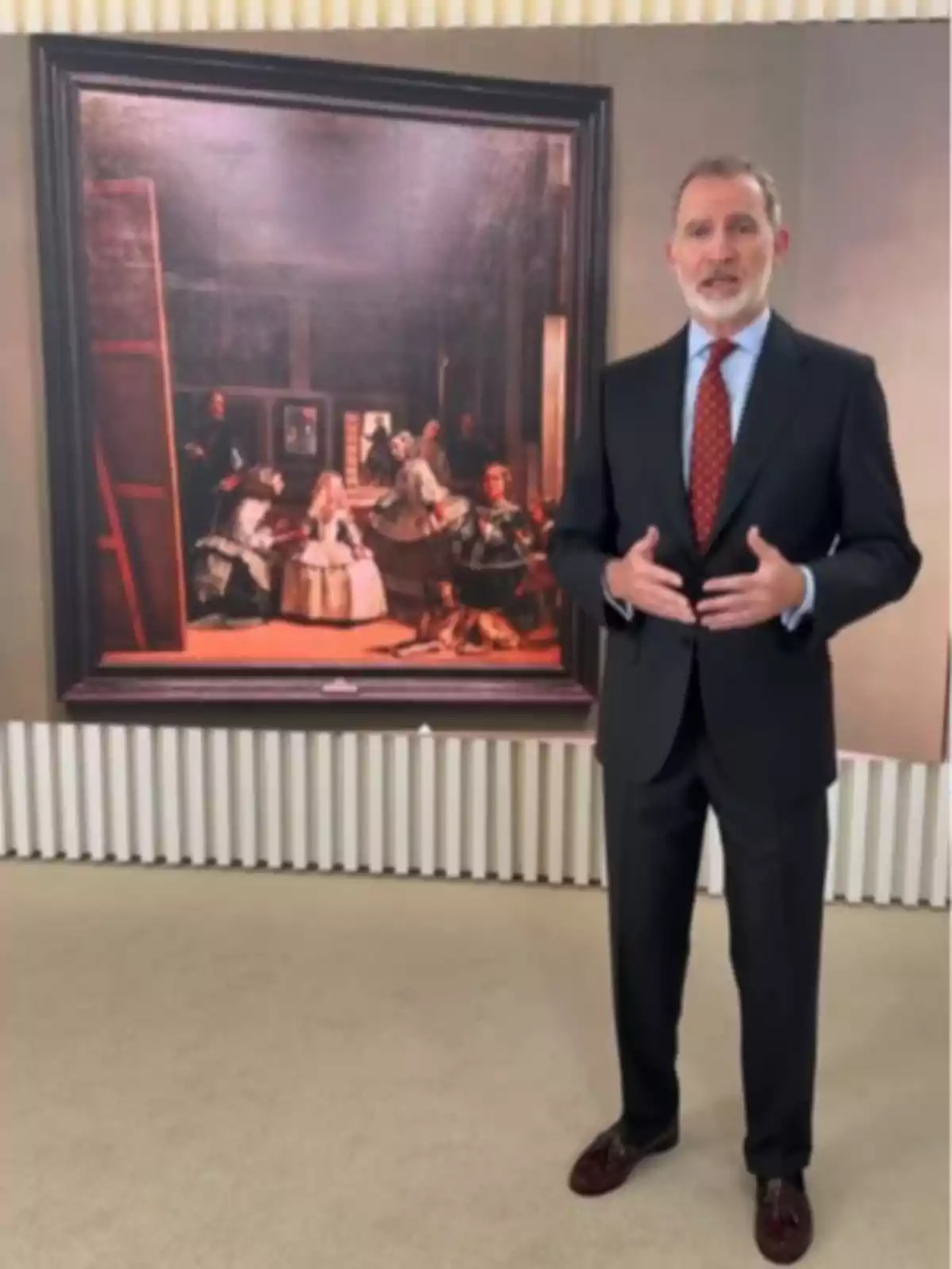 El rei Felip VI amb vestit fosc i corbata vermella posant davant del quadre Las Meninas de Velázquez El rei Felip VI amb vestit fosc i corbata vermella posant davant del quadre Las Meninas de Velázquez