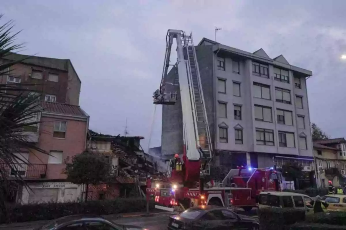 Un camió de bombers amb una escala estesa està en acció davant d'un edifici danyat a Santander, mentre els bombers treballen al lloc.