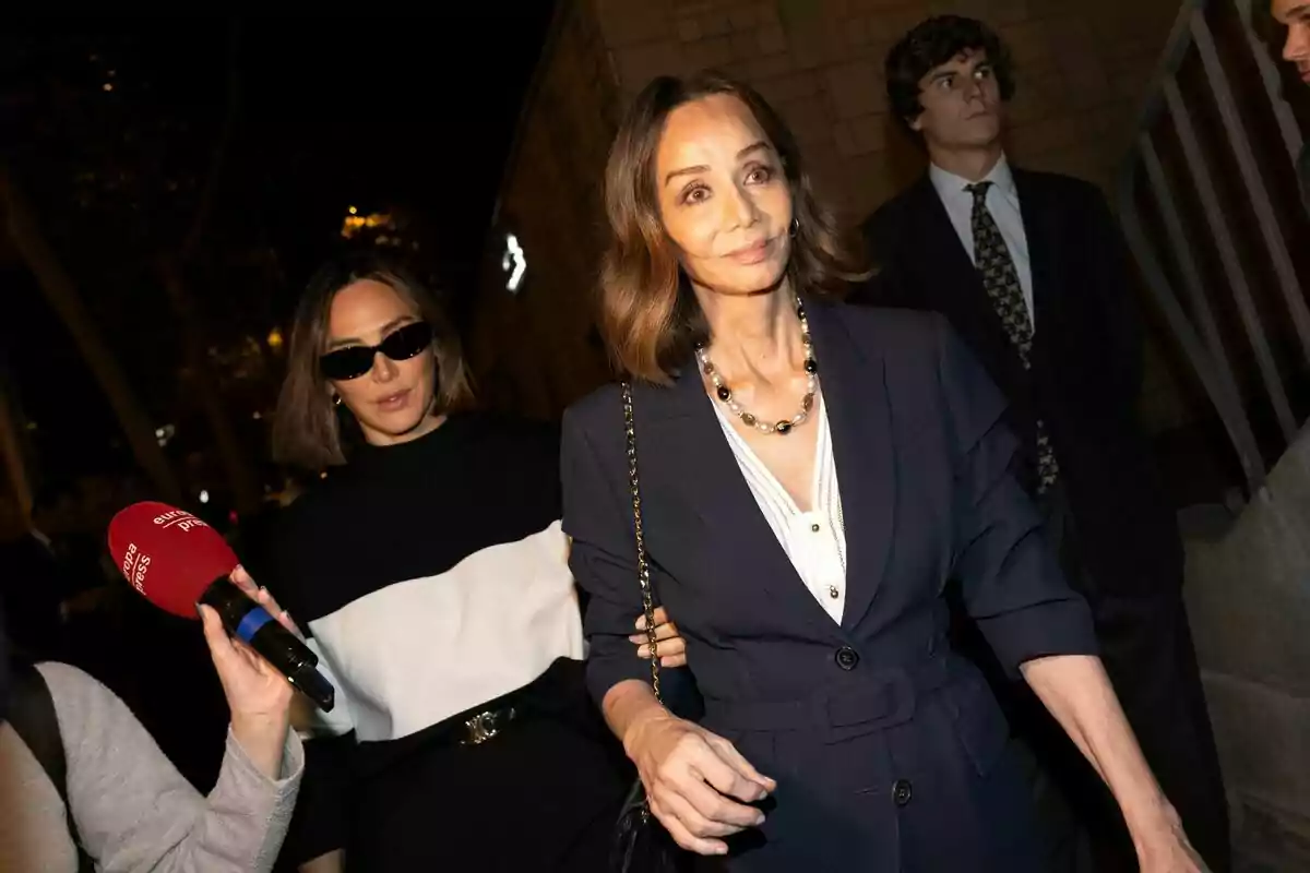 Tamara Falcó i Isabel Preysler caminant, una amb ulleres de sol i l'altra amb un collaret de perles, mentre una persona sosté un micròfon vermell d'Europa Press davant seu. Tamara Falcó i Isabel Preysler caminant, una amb ulleres de sol i l'altra amb un collaret de perles, mentre una persona sosté un micròfon vermell d'Europa Press davant seu.