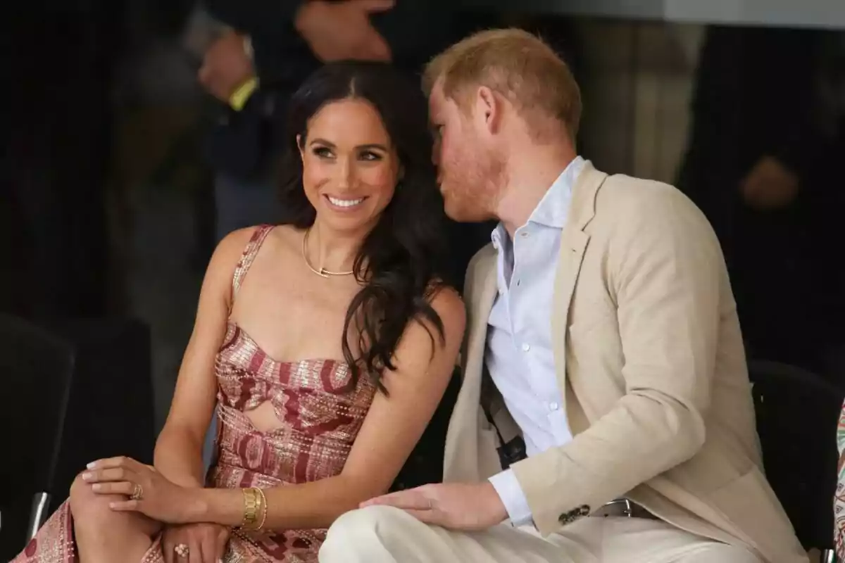 Foto del príncipe Harry hablándole a la oreja a Meghan Markle durante la presentación del grupo de teatro Danza Pies del Sol.