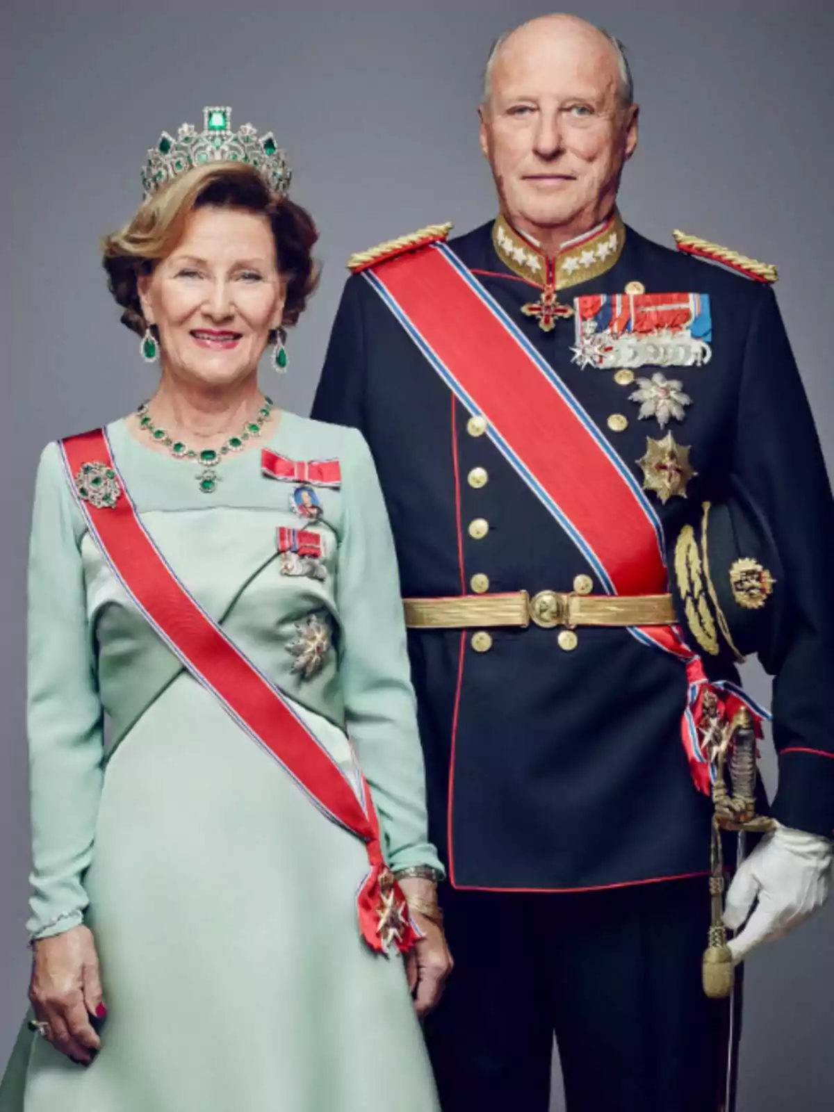 La reina Sònia i el rei Harald de Noruega vestits amb vestits formals i condecoracions, la dona porta una tiara i un vestit verd clar, mentre que l'home vesteix un uniforme militar fosc amb medalles i una banda vermella. La reina Sònia i el rei Harald de Noruega vestits amb vestits formals i condecoracions, la dona porta una tiara i un vestit verd clar, mentre que l'home vesteix un uniforme militar fosc amb medalles i una banda vermella.