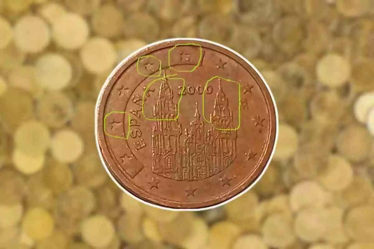 Moneda d'un cèntim d'euro d'Espanya de l'any 2000 amb la Catedral de Santiago de Compostel·la al centre i estrelles al voltant sobre un fons de monedes desenfocades.