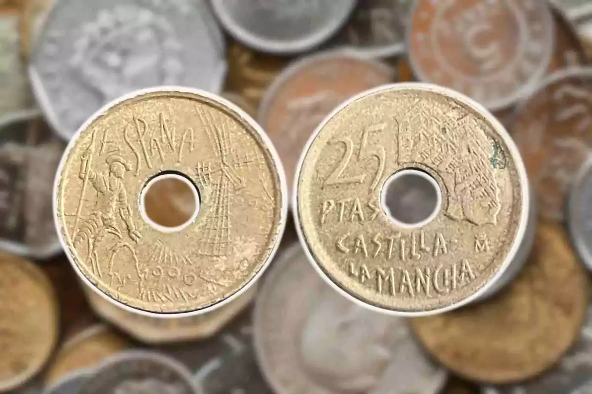 Monedes antigues de 25 pessetes d'Espanya amb un forat al centre i al fons d'altres monedes desenfocades. Monedes antigues de 25 pessetes d'Espanya amb un forat al centre i al fons d'altres monedes desenfocades.
