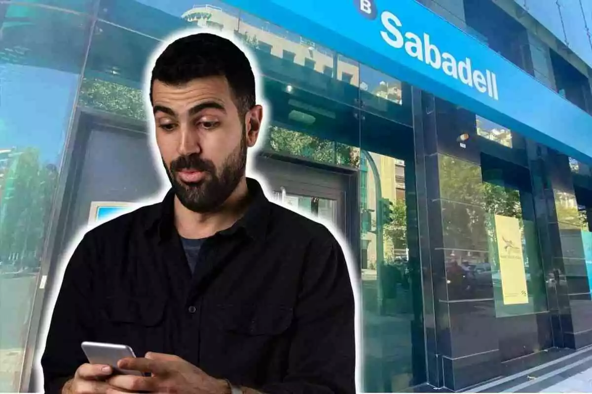 Un home amb expressió sorpresa mira el telèfon mòbil davant d'una sucursal del Banc Sabadell.