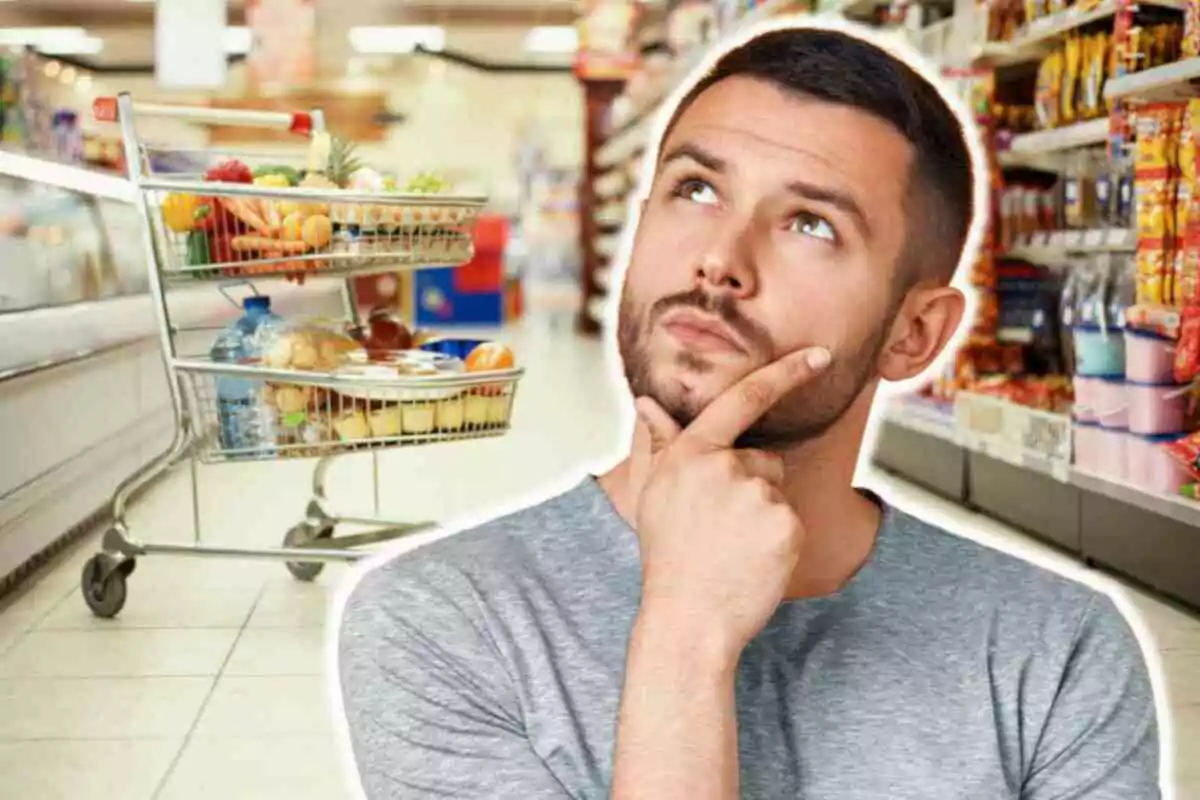 Home pensatiu en un supermercat amb un carretó de compres ple d'aliments.