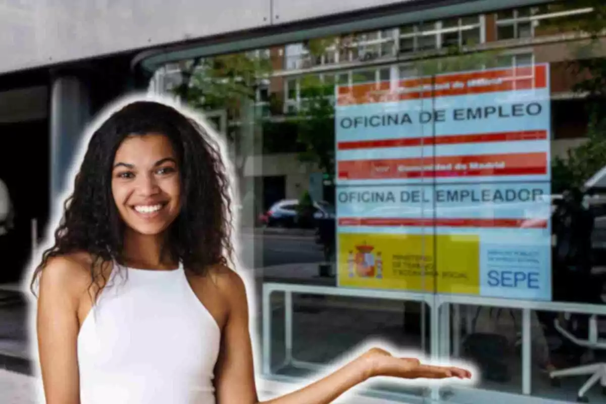 Una dona somrient amb una samarreta sense mànigues blanca està dreta davant d'una oficina d'ocupació a Madrid, Espanya. L'oficina té un cartell a la finestra que diu "OFICINA D'OCUPACIÓ" i "OFICINA DE L'EMPLEADOR", juntament amb logotips del Ministeri de Treball i Economia Social i del SEPE (Servei Públic d'Ocupació Estatal). Sembla que la dona està assenyalant cap a l'oficina amb una mà estesa.