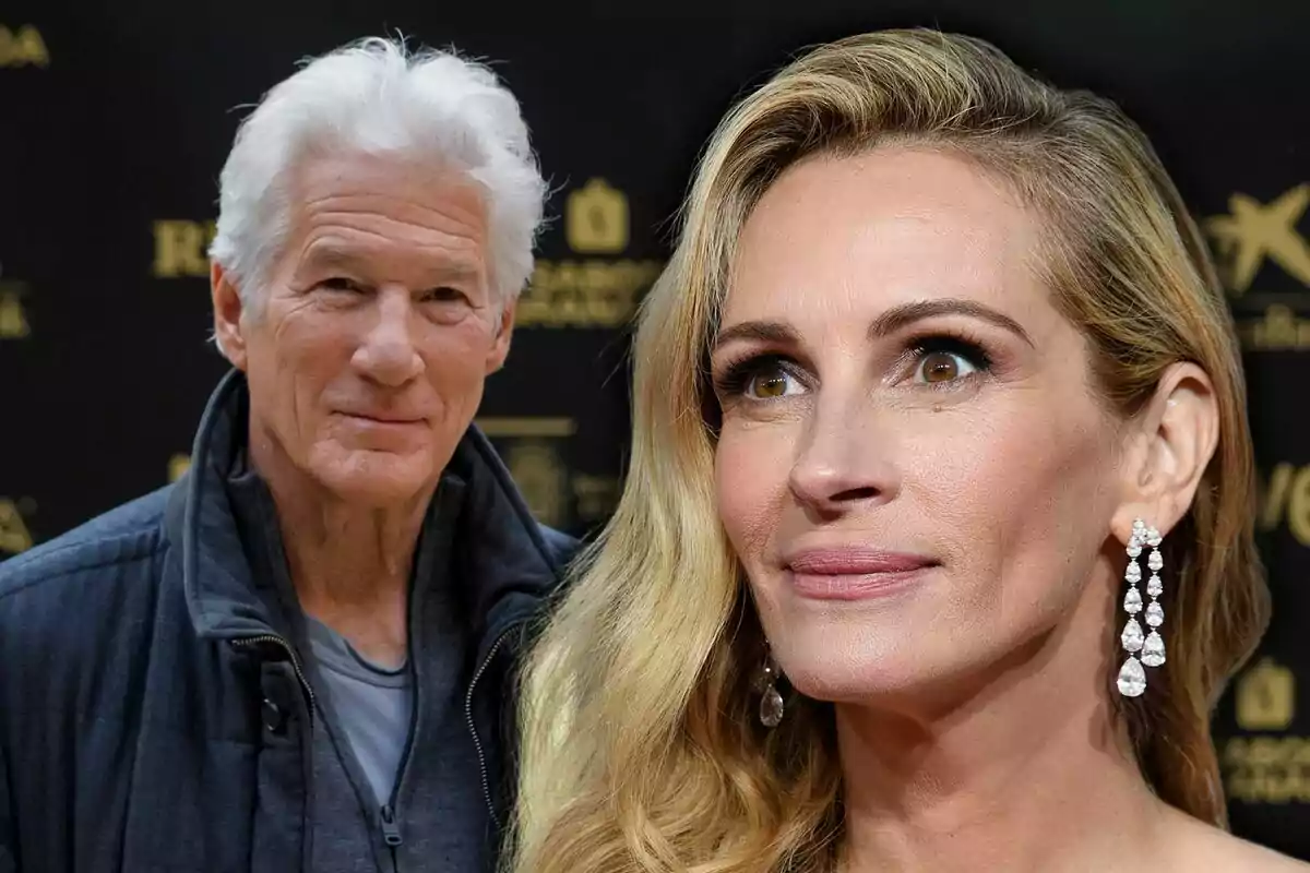 A gray-haired man and a blonde woman with long earrings pose together at an elegant event with a dark background.