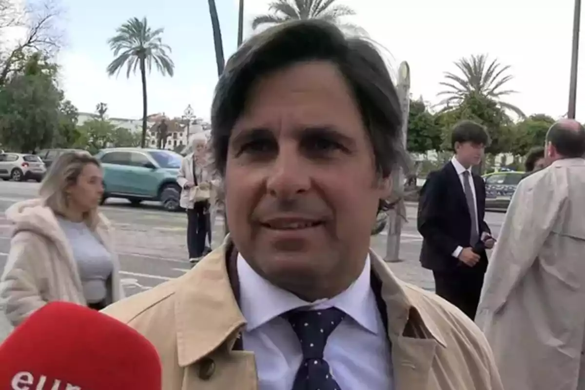 Fran Rivera amb jaqueta beix i corbata blava amb llunes és entrevistat al carrer mentre persones caminen i cotxes passen de fons. Fran Rivera amb jaqueta beix i corbata blava amb llunes és entrevistat al carrer mentre persones caminen i cotxes passen de fons.