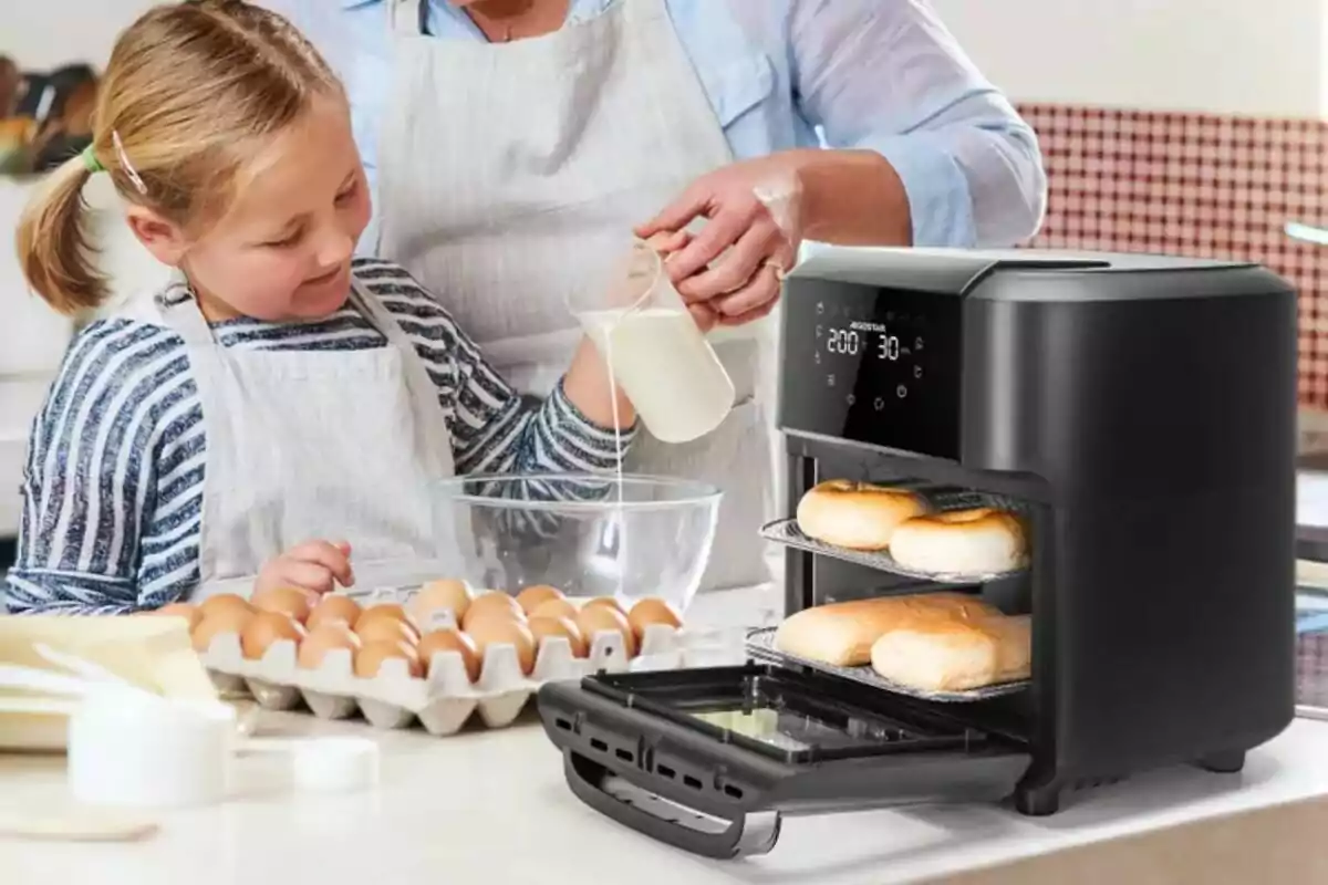 Una niña y un adulto cocinan juntos en una cocina, mientras una freidora de aire de Leroy Merlin está horneando panecillos.