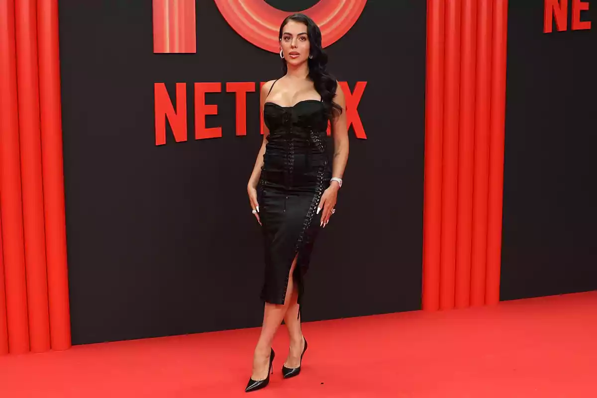 Georgina Rodríguez amb vestit negre elegant i talons posant sobre una catifa vermella amb fons de Netflix Georgina Rodríguez amb vestit negre elegant i talons posant sobre una catifa vermella amb fons de Netflix