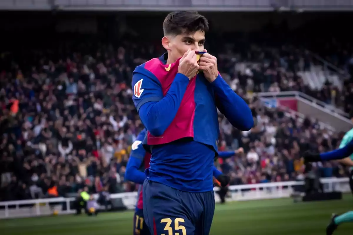 A player celebrates a goal by kissing the badge on his jersey in front of a crowd at the stadium.