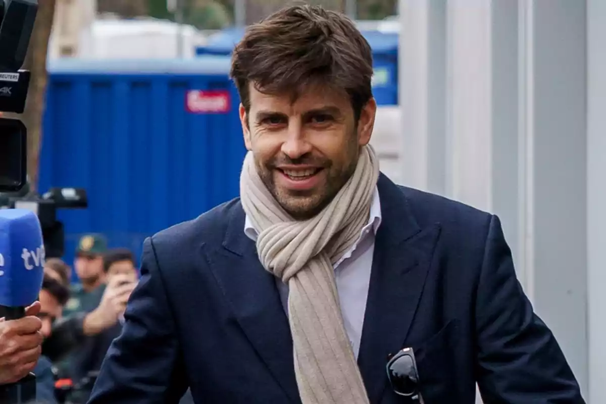 Gerard Piqué smiling with a beard and clear scarf carries a dark suit while walking outdoors. Gerard Piqué smiling with a beard and clear scarf carries a dark suit while walking outdoors.
