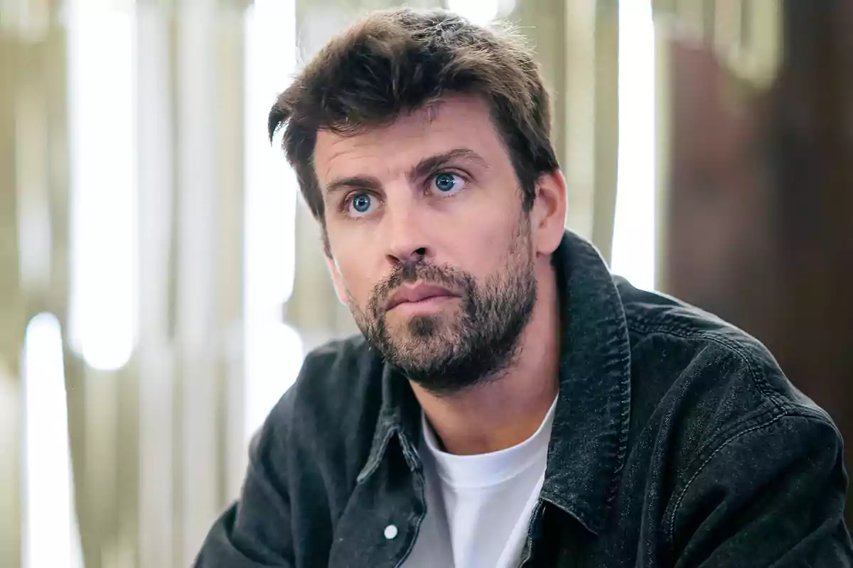 Gerard Piqué looks thoughtfully ahead, wearing a dark jacket over a white t-jersey, with a blurred background. Gerard Piqué looks thoughtfully ahead, wearing a dark jacket over a white t-jersey, with a blurred background.