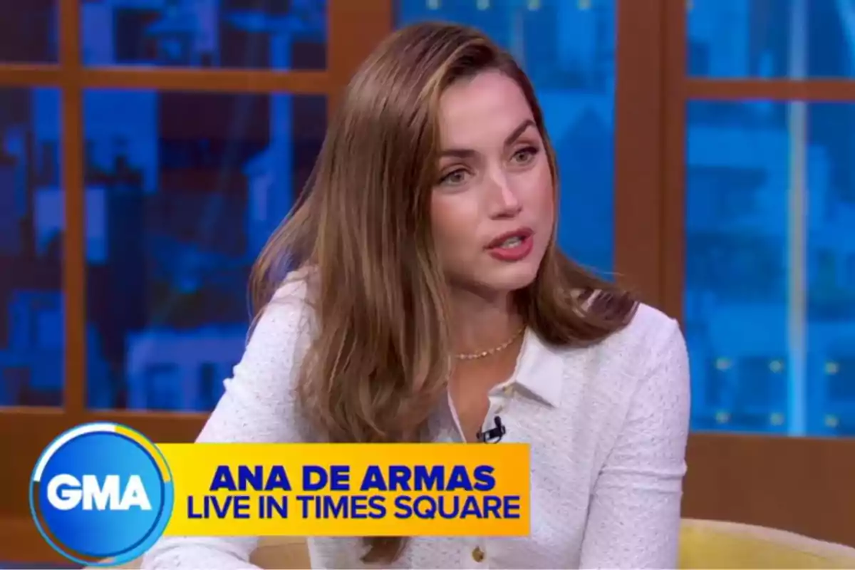 Ana de Armas is sitting on a television set, wearing a white blouse, while speaking during an interview. Screenshot from 'Good Morning America'. Ana de Armas is sitting on a television set, wearing a white blouse, while speaking during an interview. Screenshot from 'Good Morning America'.
