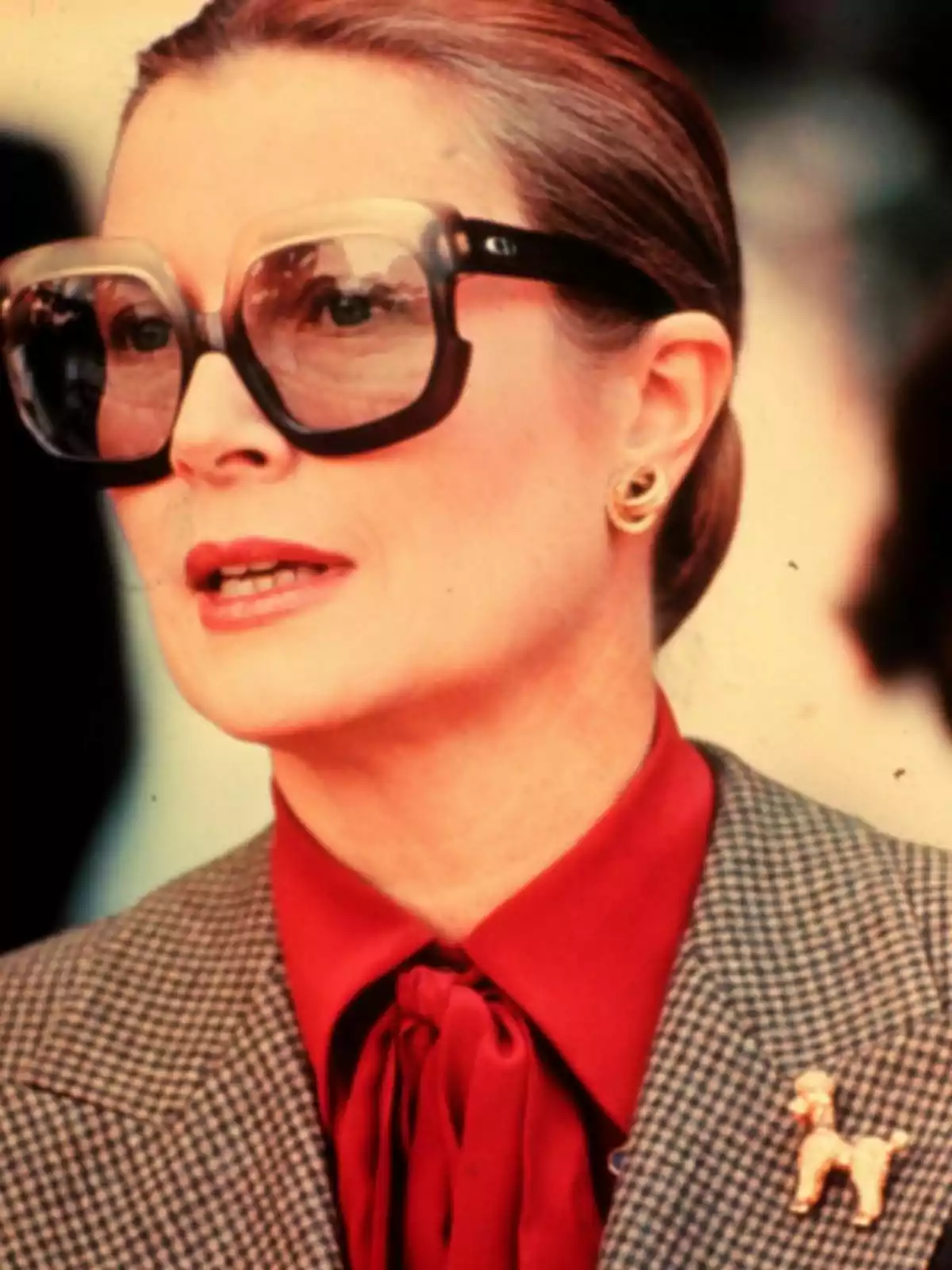 Grace Kelly amb ulleres grans i cabell recollit, vestint una brusa vermella i jaqueta de quadres. Grace Kelly amb ulleres grans i cabell recollit, vestint una brusa vermella i jaqueta de quadres.