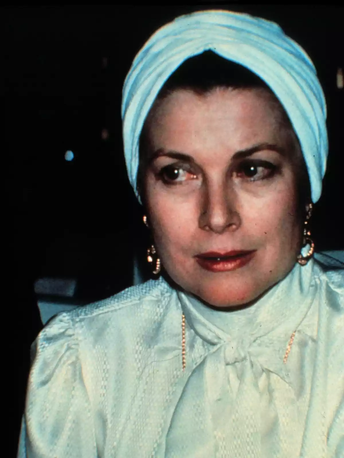 Grace Kelly in a white turban and light blouse looks to the side. Grace Kelly in a white turban and light blouse looks to the side.