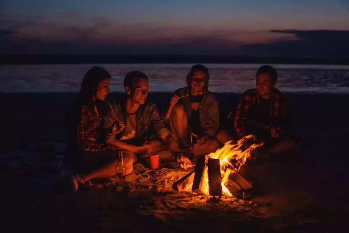 Un grup d'amics a la platja de nit asseguts al voltant d'una petita foguera