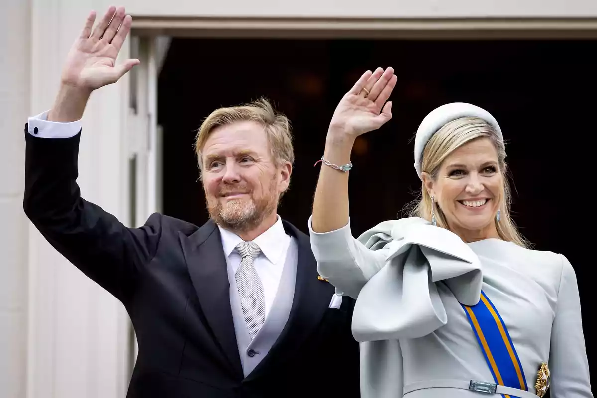 Guillerm i Máxima d’Holanda, elegantment vestida, saluda somrient amb la mà aixecada des d’un balcó.