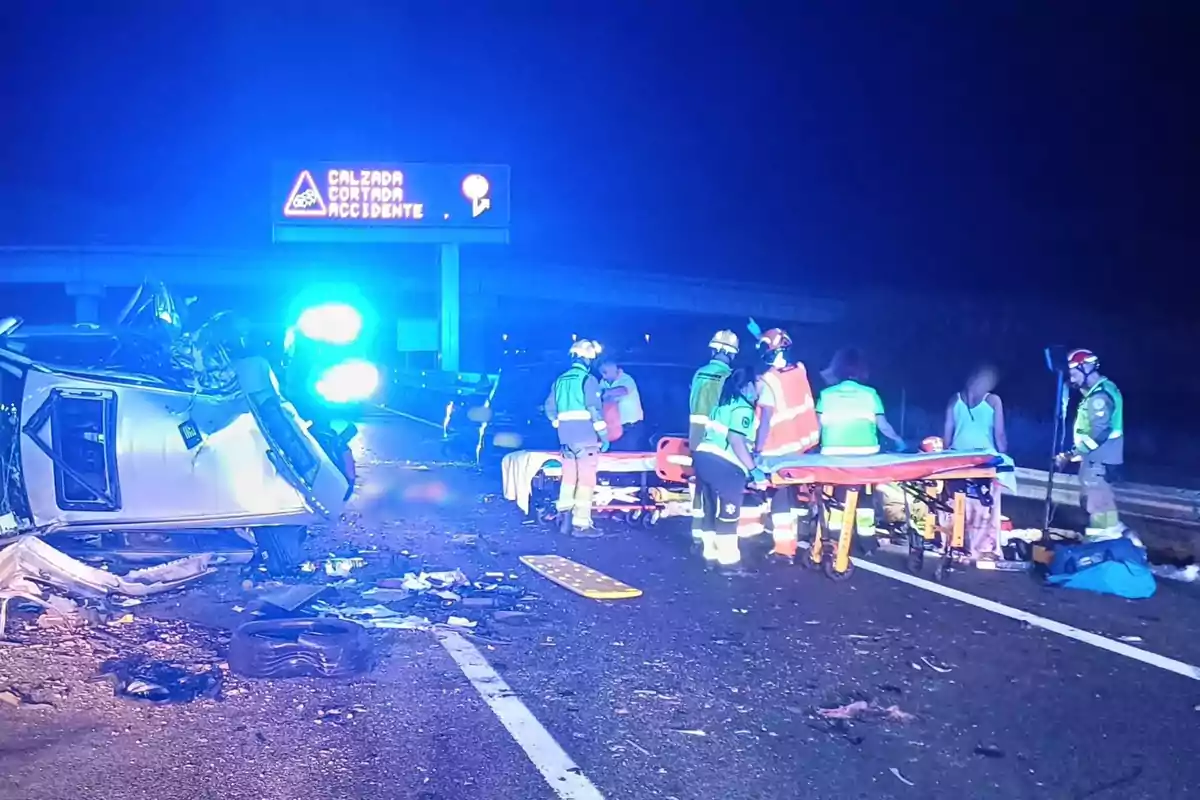 Accident de trànsit nocturn a una carretera amb un cotxe bolcat i equips d'emergència atenent els ferits.